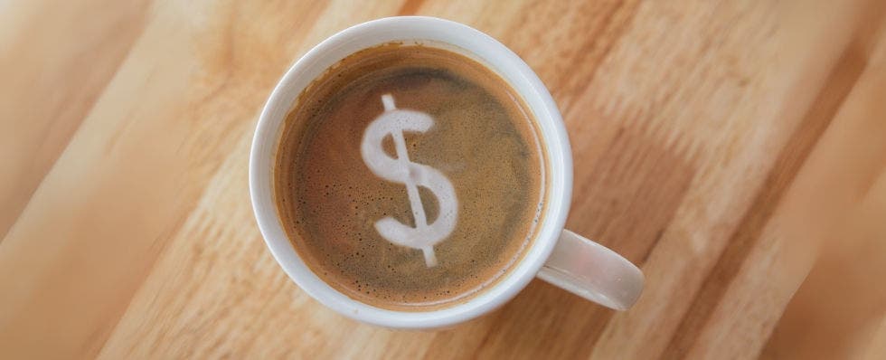 Dollar sign in cup of coffee with in a white cup on wooden background.